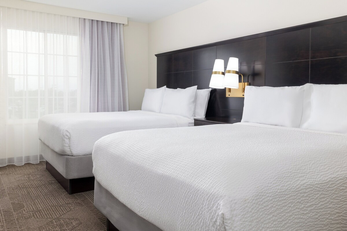 A hotel room with two beds, a dark headboard, and a nightstand with lamps.