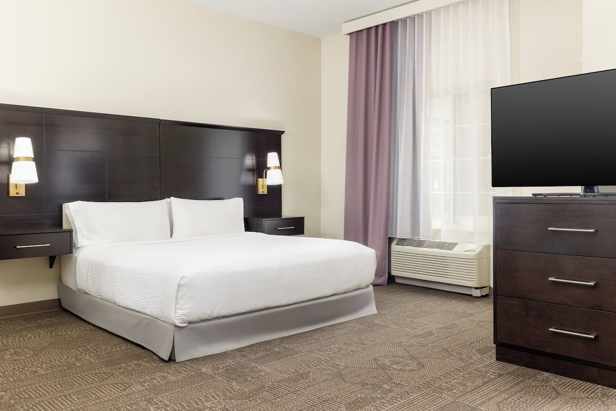Habitación de hotel con cama, mesitas de noche, televisor de pantalla plana, cómoda y aire acondicionado.