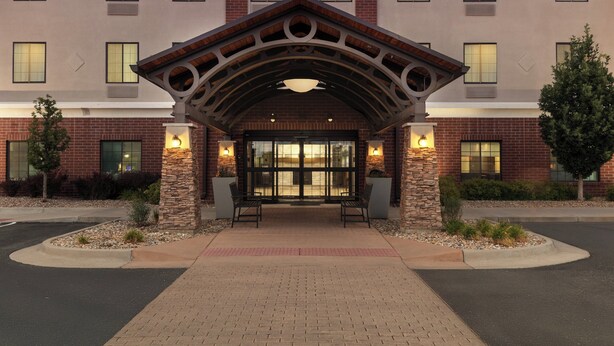 A hotel entrance with a brick facade, a covered entrance area, and two benches. - Staybridge Suites Denver-Central Park by IHG (Denver)