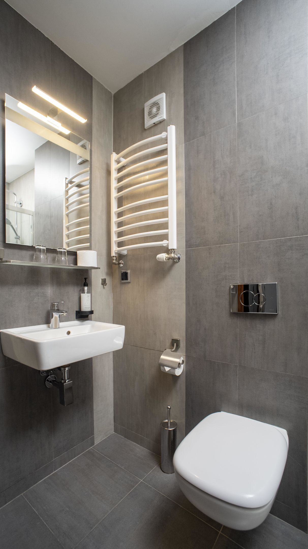 A modern bathroom with a white sink, mirror, and toilet.