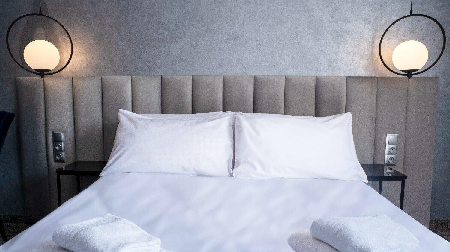 Une chambre d’hôtel avec un grand lit, deux tables de chevet et deux lampes fixées au mur.
