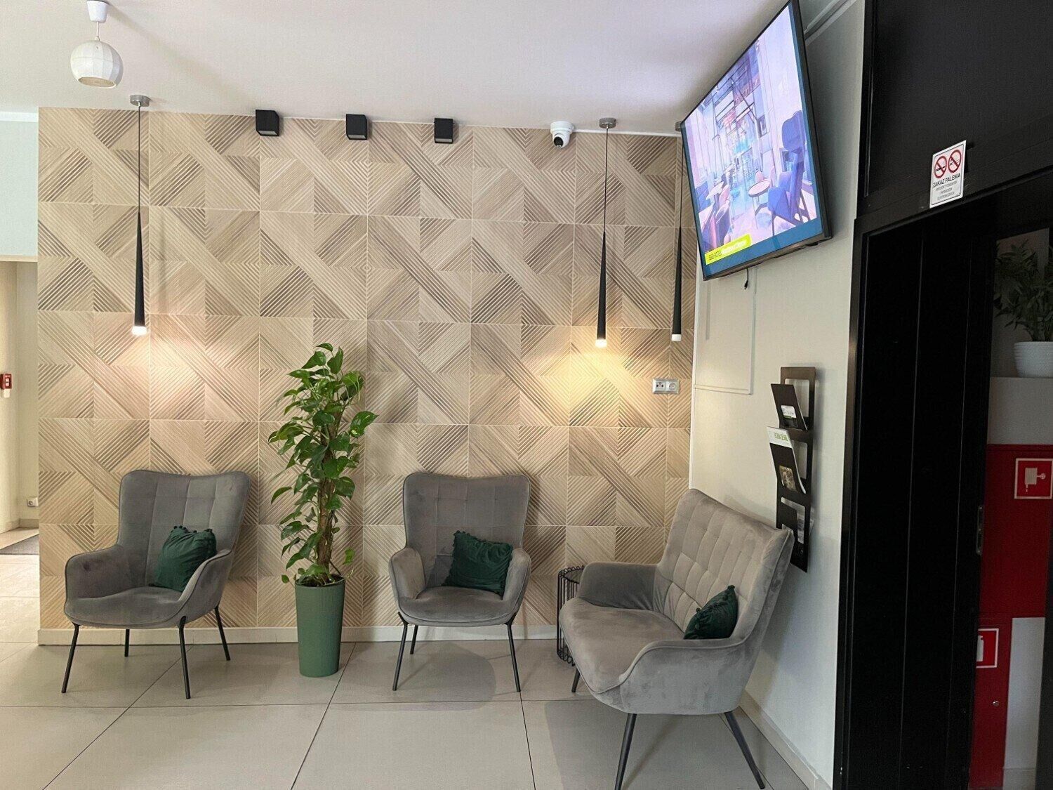 A waiting area with three grey chairs, a potted plant, and a TV mounted on the wall.