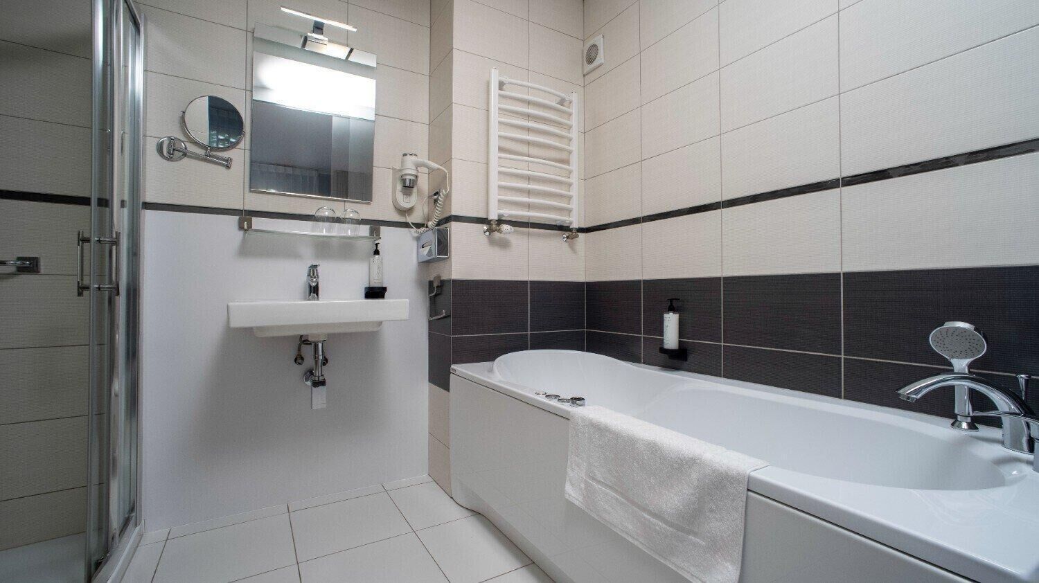 A modern bathroom with a glass shower enclosure, a white sink, a large bathtub, and a towel hanging on the tub.