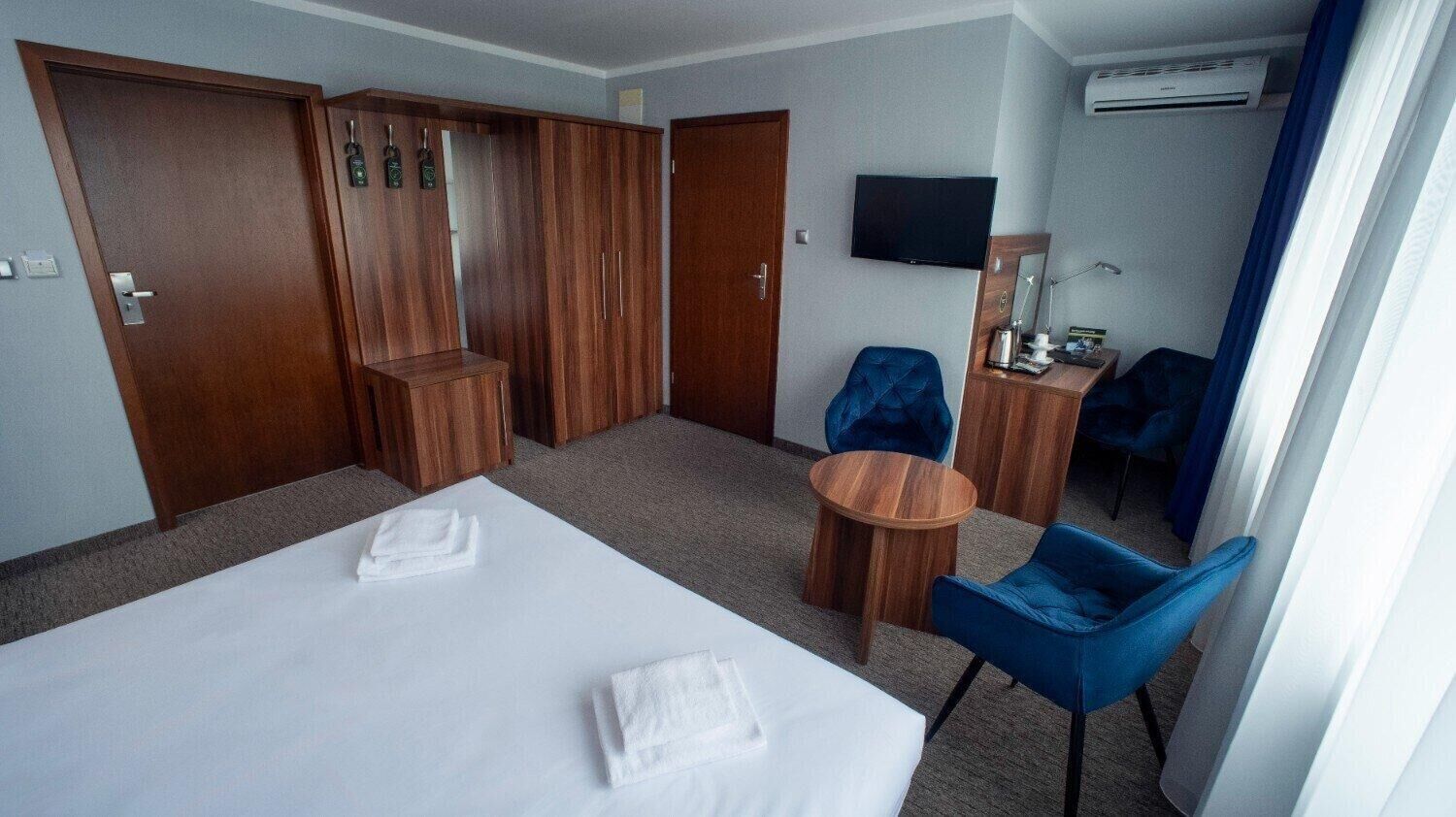 A hotel room with two beds, a desk, a chair, a TV, and a wardrobe.