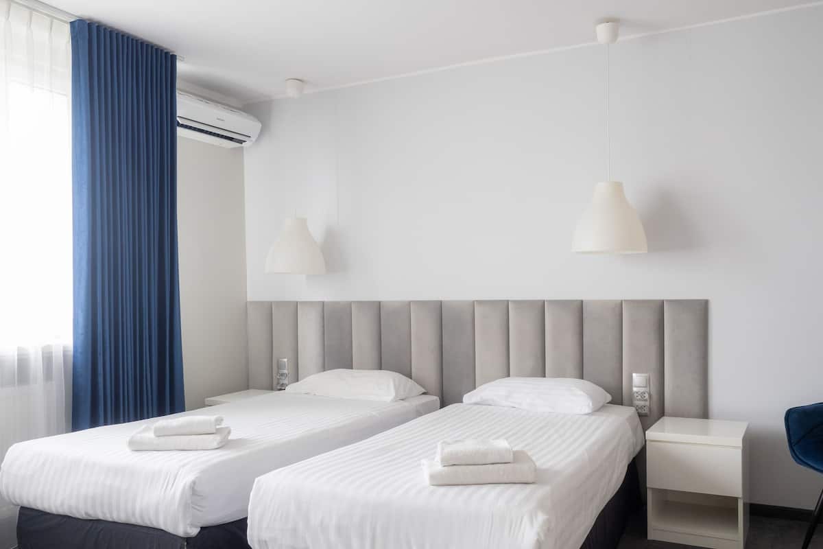 Ein Hotelzimmer mit zwei Betten, einem blauen Vorhang, einer Klimaanlage und einem Sessel.