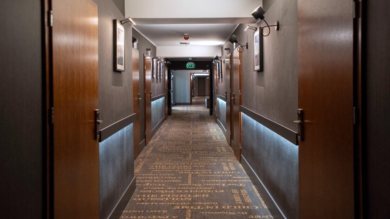 Un pasillo de hotel con puertas de madera, una alfombra estampada y cuadros enmarcados en las paredes.