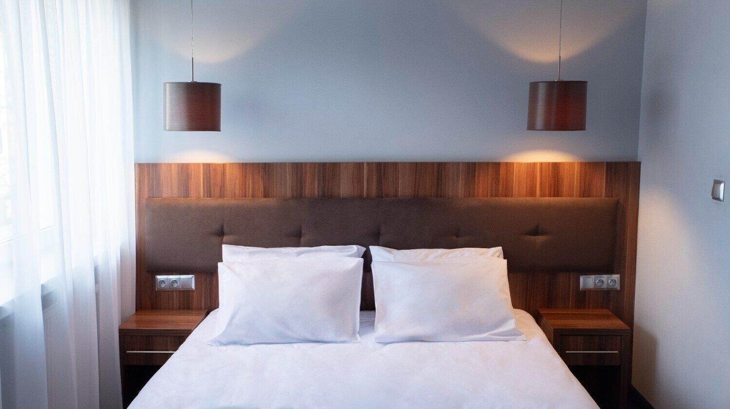 Una habitación de hotel con una cama grande, dos mesitas de noche, un cabecero de madera y dos lámparas de pared.