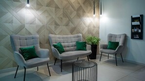 Un área de espera moderna con tres sillones tapizados de color gris, cada uno con un cojín verde, y una mesa de metal negro en el centro.