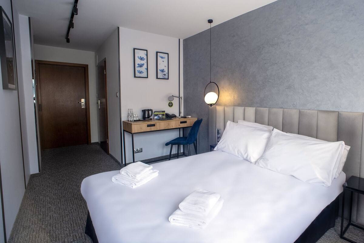 Ein Hotelzimmer mit Bett, Schreibtisch, Stuhl und Wandlampe.