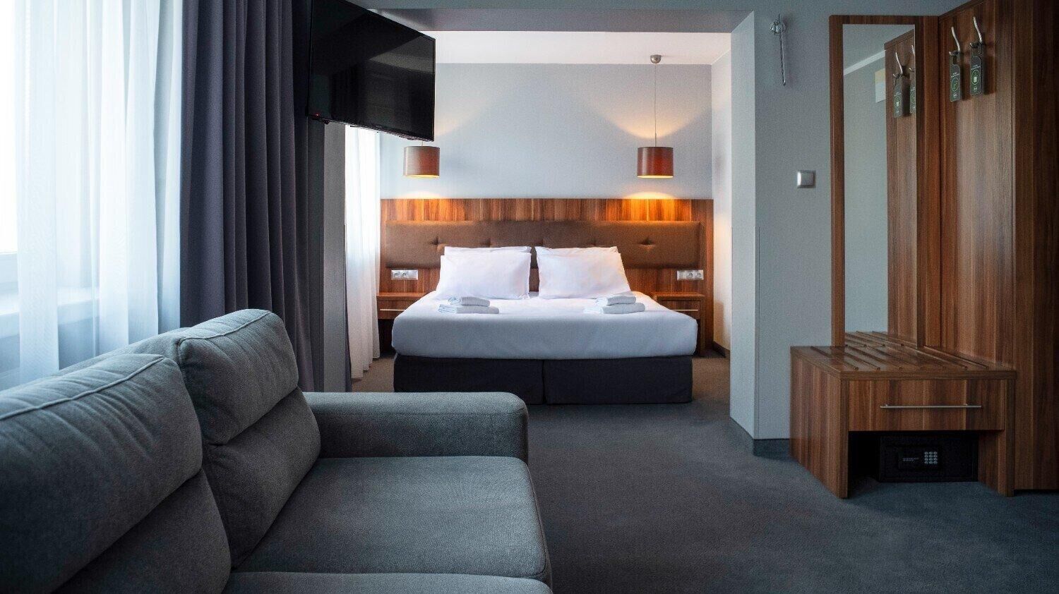Una habitación de hotel con una cama, un sofá, un televisor, un armario de madera y un espejo.