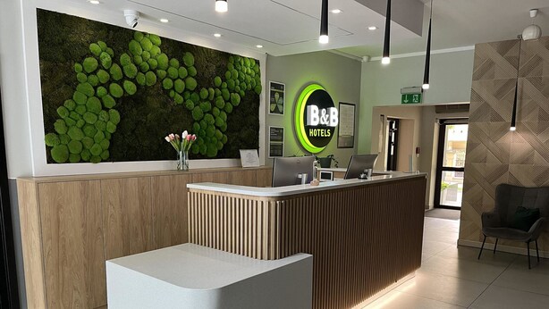 Una recepción con una pared de musgo verde, un letrero de B&B Hotels y un diseño interior moderno.