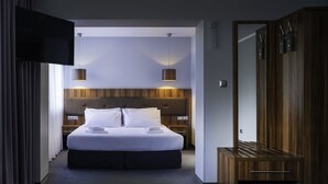 Una habitación de hotel moderna con una cama grande, cabecera de madera, dos lámparas de noche y un armario.