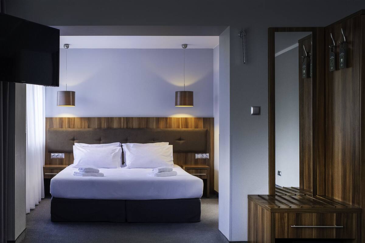 Ein modernes Hotelzimmer mit einem großen Bett, einem Holzkopfteil, zwei Nachttischlampen und einem Kleiderschrank.