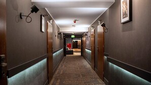 Un pasillo de hotel con piso alfombrado, puertas de madera y un letrero de salida rojo.