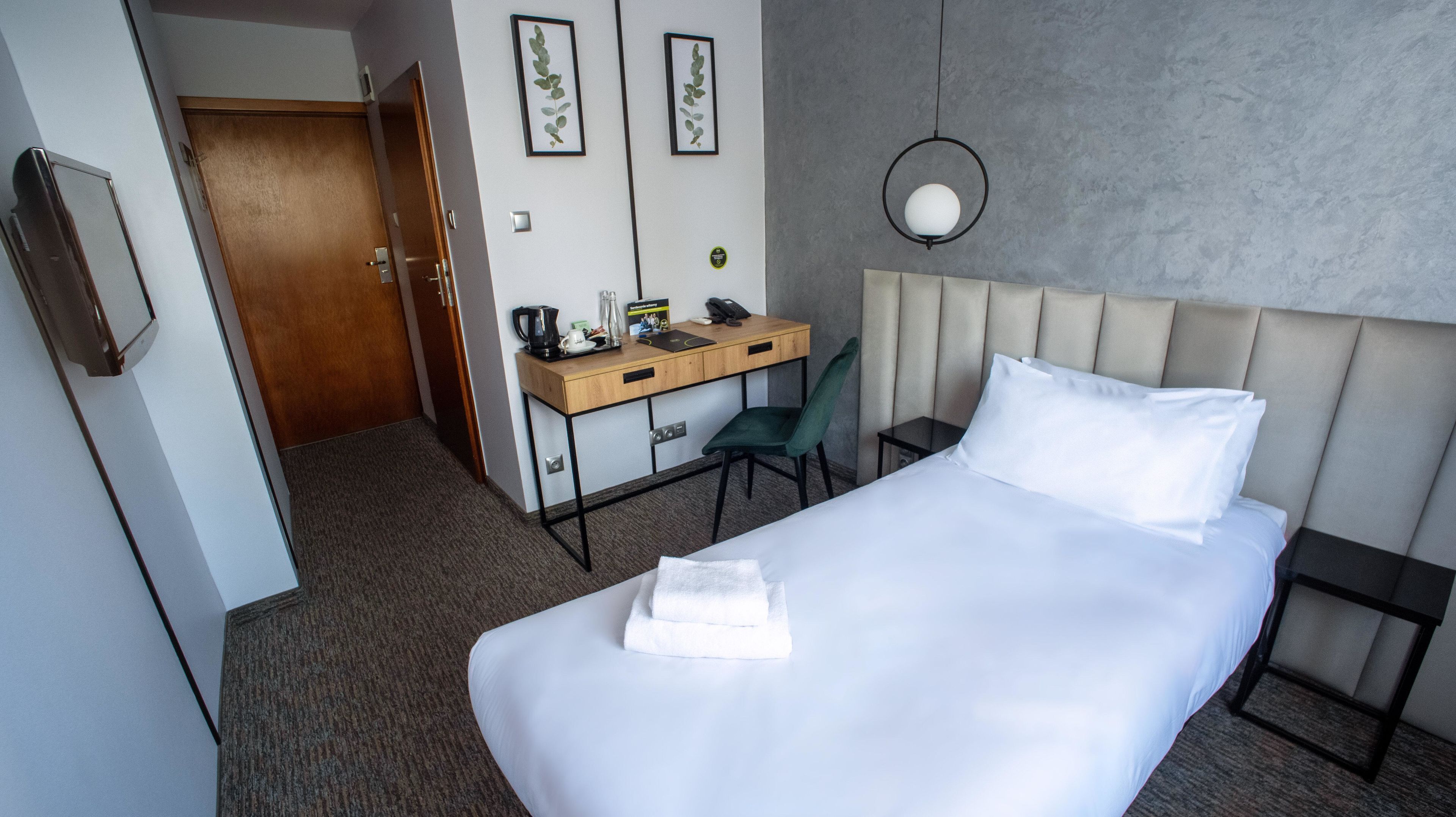 Een hotelkamer met een bed, een bureau, een stoel, een koffiezetapparaat en ingelijste foto's aan de muur.