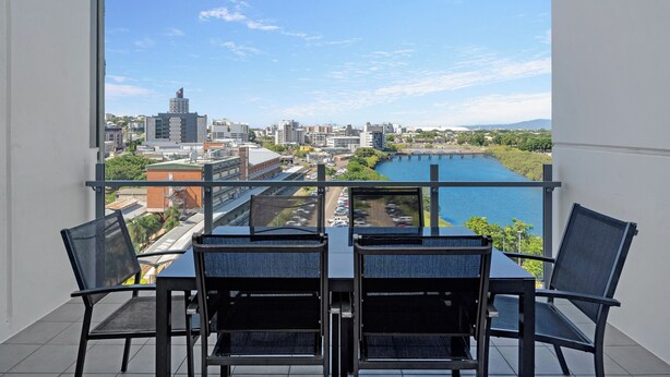 A balcony with a table and chairs, overlooking a cityscape and a river. - Islington at Central (Townsville)