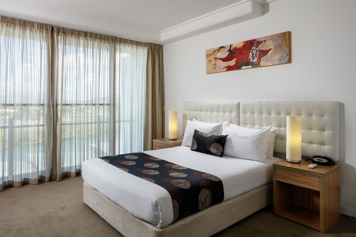 A hotel room with a large bed, a headboard, two bedside tables with lamps, a nightstand, and a painting on the wall.