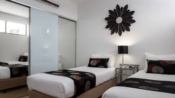 Habitación de hotel con dos camas, un espejo grande, un adorno floral en la pared y una mesita de noche con lámpara.