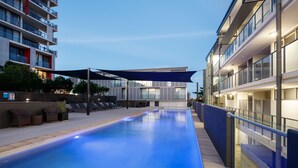 A modern pool area with lounge chairs and a shaded canopy, surrounded by high-rise buildings. - Islington at Central (Townsville)