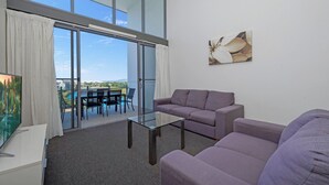 A modern living room with a glass coffee table, two sofas, a flat-screen TV, and a balcony with a view of the city. - Islington at Central (Townsville)