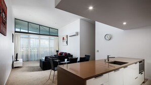 A modern kitchen with a large island, a dining area with a sofa and chairs, and a large window with sheer curtains. - Islington at Central (Townsville)