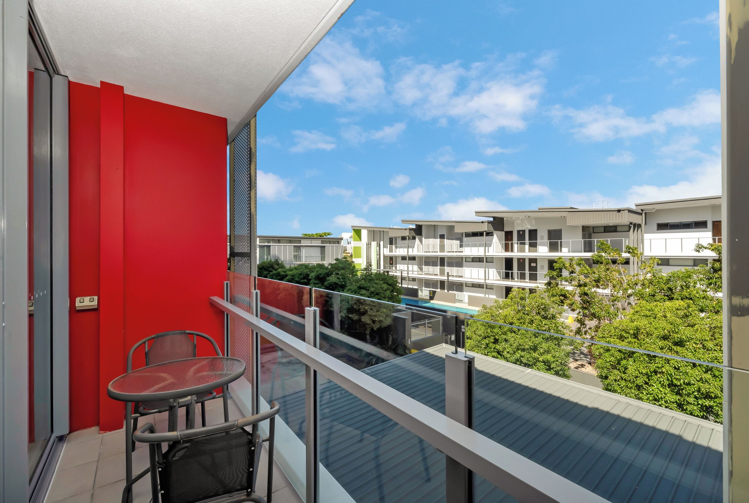 A balcony with a red wall, a glass table, and a chair.