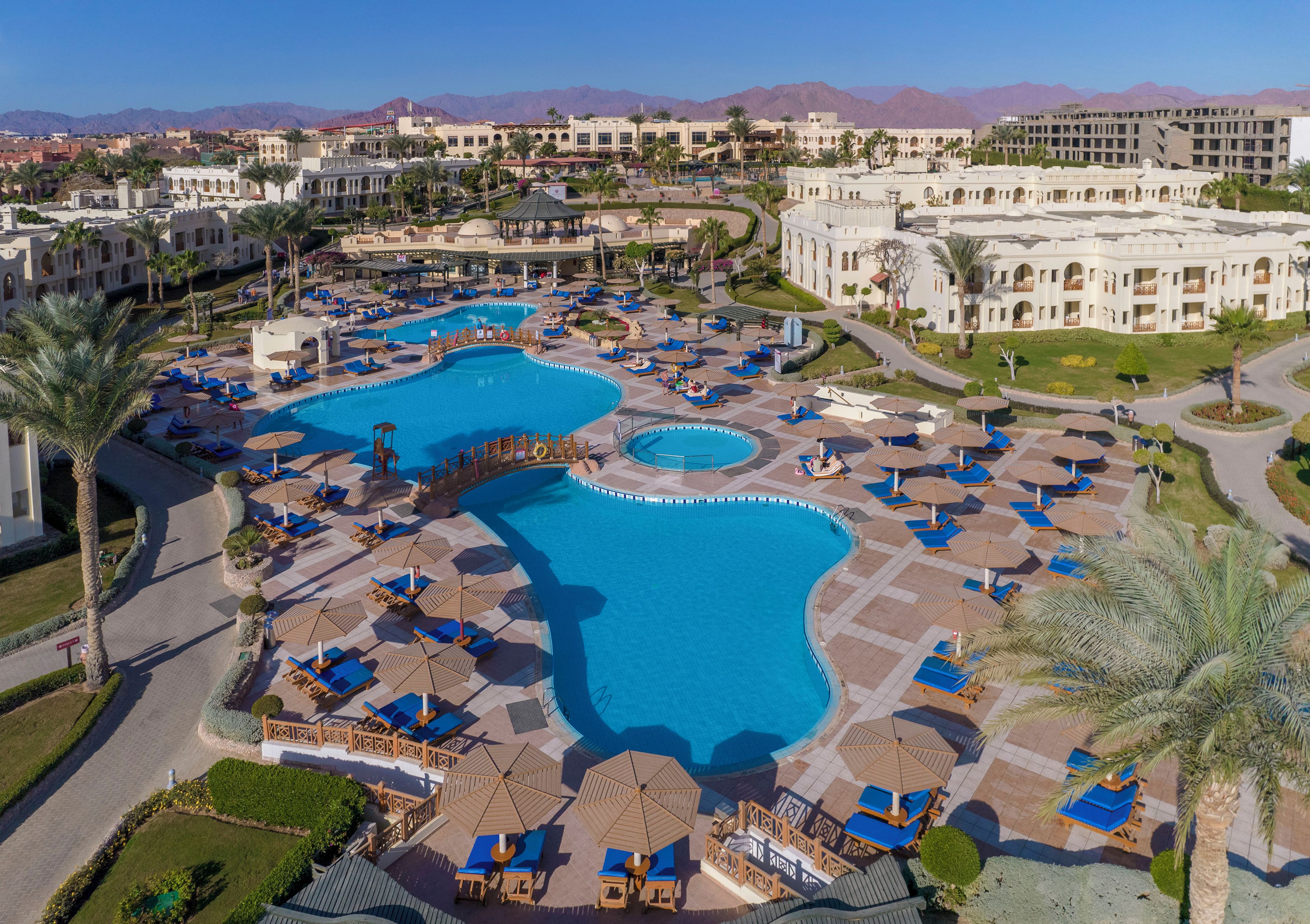 A resort with multiple swimming pools, sun loungers, and palm trees.