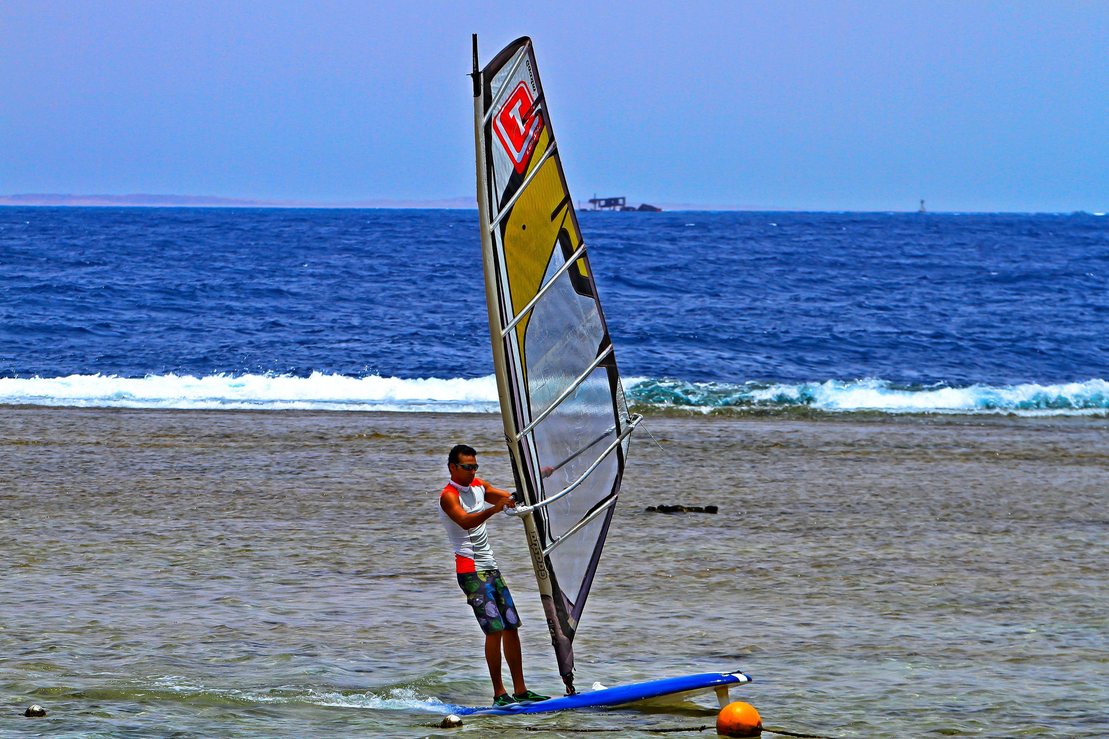 Une personne pratiquant la planche à voile sur une plage, avec l’océan en arrière-plan.