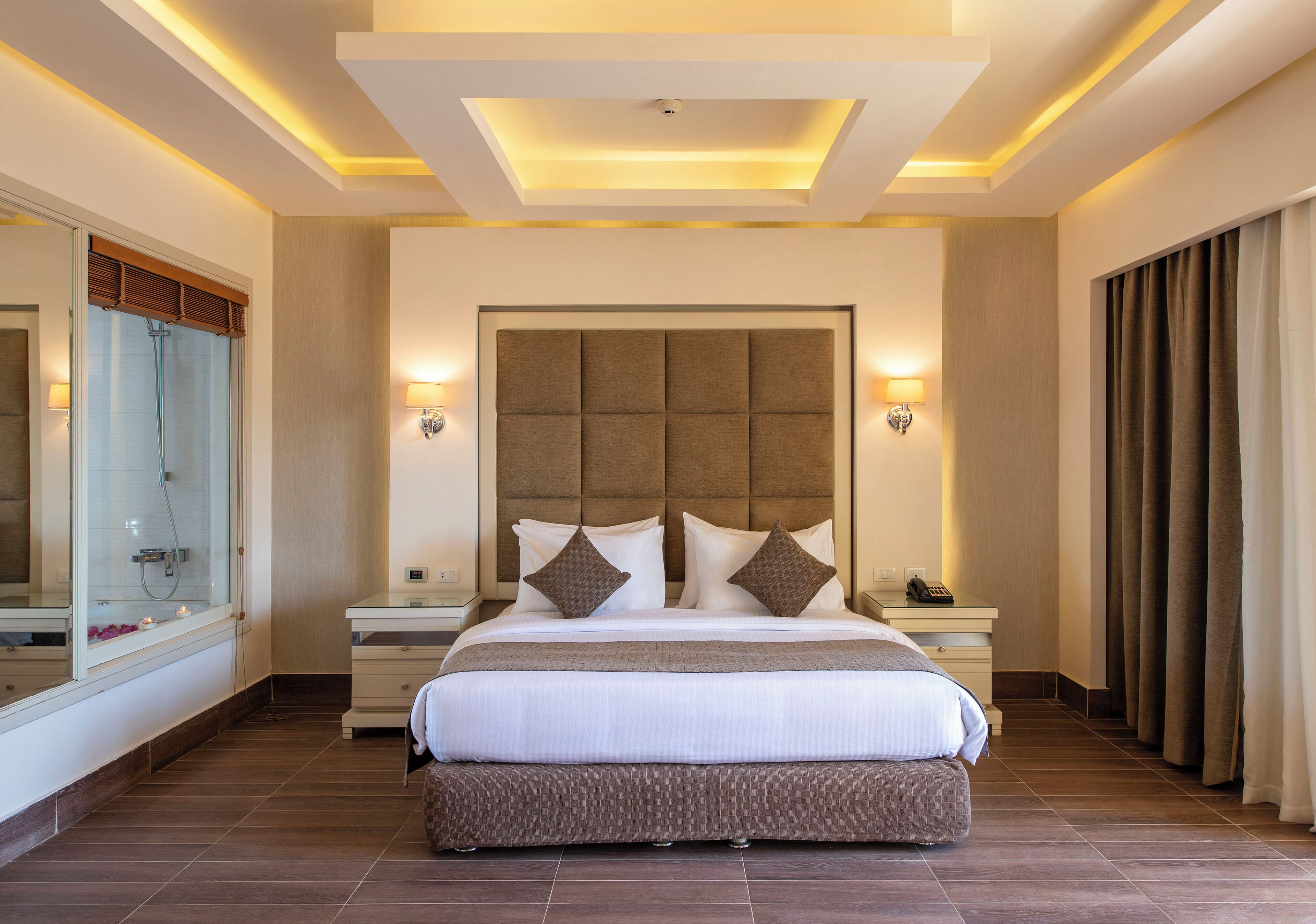 Habitación de hotel moderna con una cama grande, dos mesitas de noche, un tocador, un espejo amplio y un baño con ducha e inodoro.