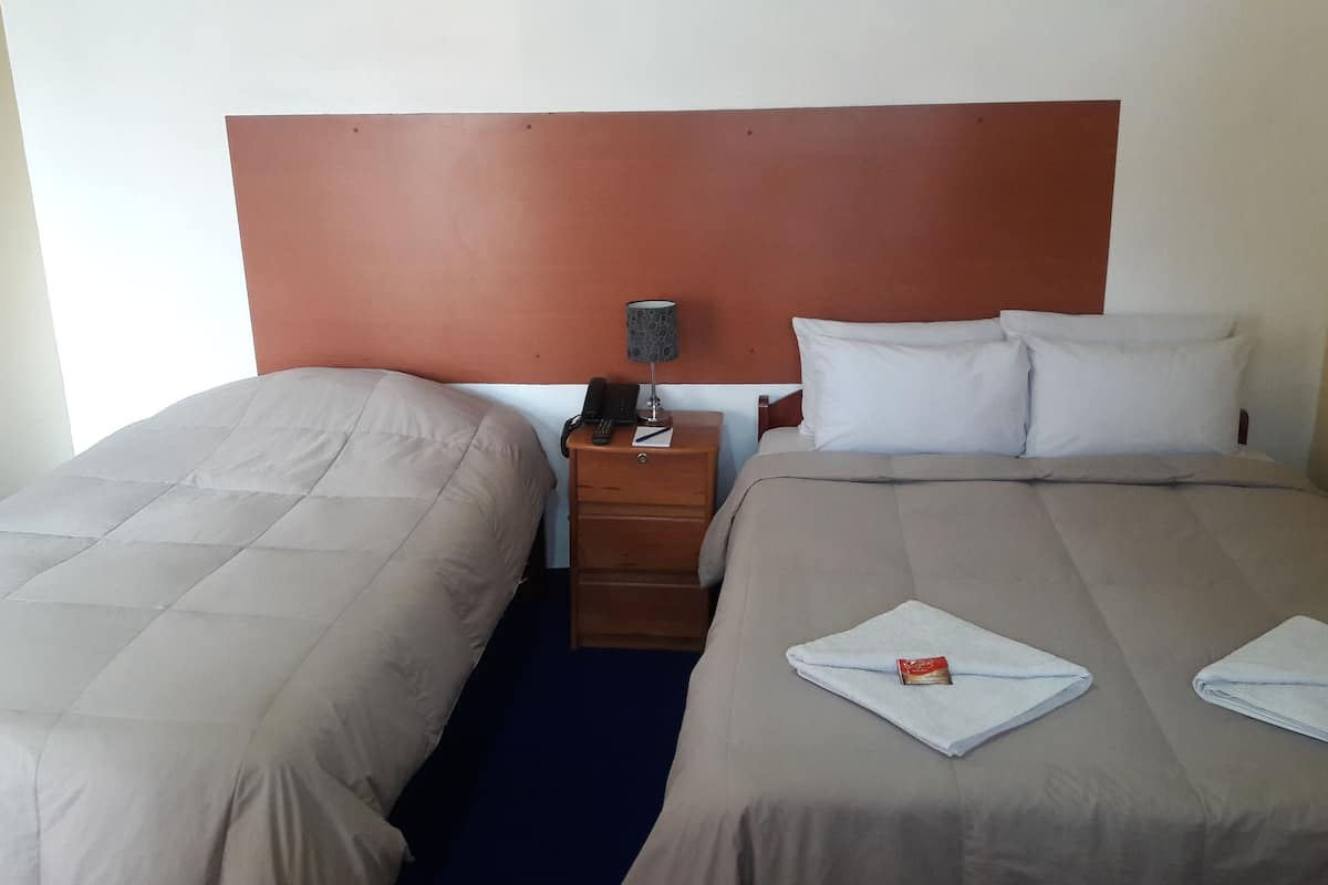 A hotel room with two beds, a nightstand with a lamp, a phone, and a small table with a book.