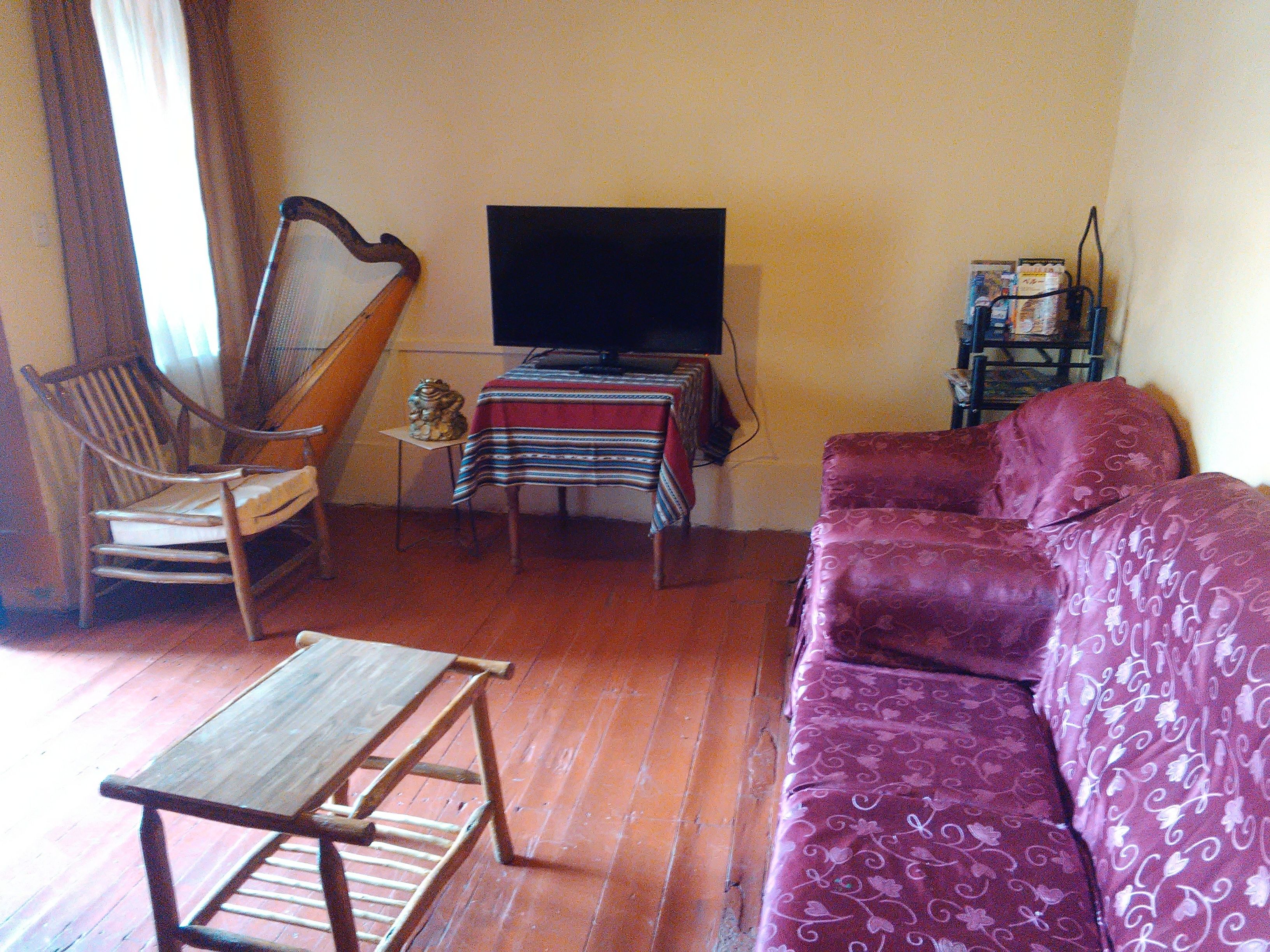 A living room with a wooden table, a cushioned sofa, a television, and a small table with a patterned tablecloth.