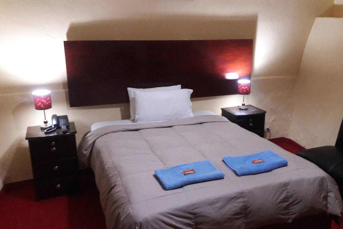 A hotel room with a bed, two bedside tables, a chair, and a headboard.