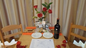 A table with a map, a bottle of wine, two empty glasses, and a vase with red roses. - Kurumi (Cusco)