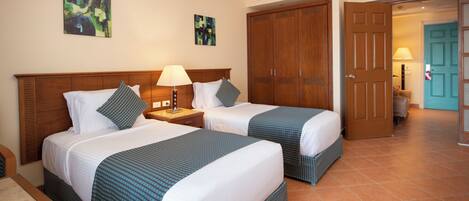 A hotel room with two beds, a wooden wardrobe, a door leading to another room, and artwork on the walls.