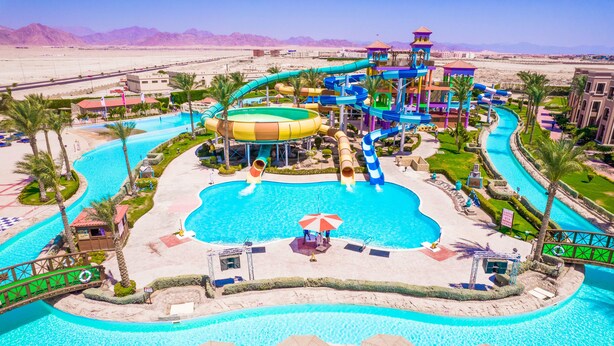 Een waterpark met meerdere glijbanen en zwembaden, omringd door palmbomen en een woestijnlandschap.