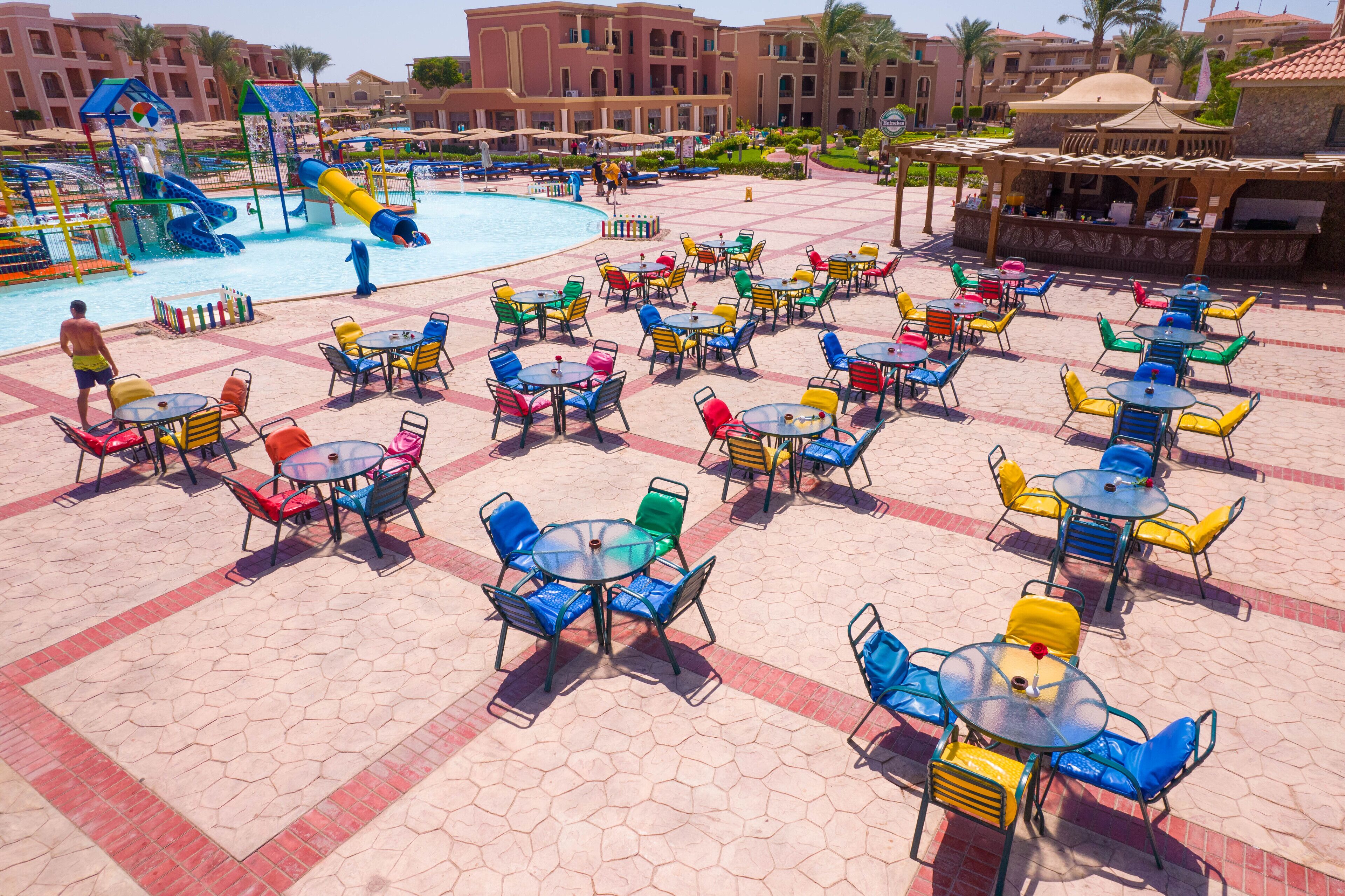 Zona de piscina en un resort con sillas y mesas coloridas, un tobogán acuático y una zona de estar cubierta.