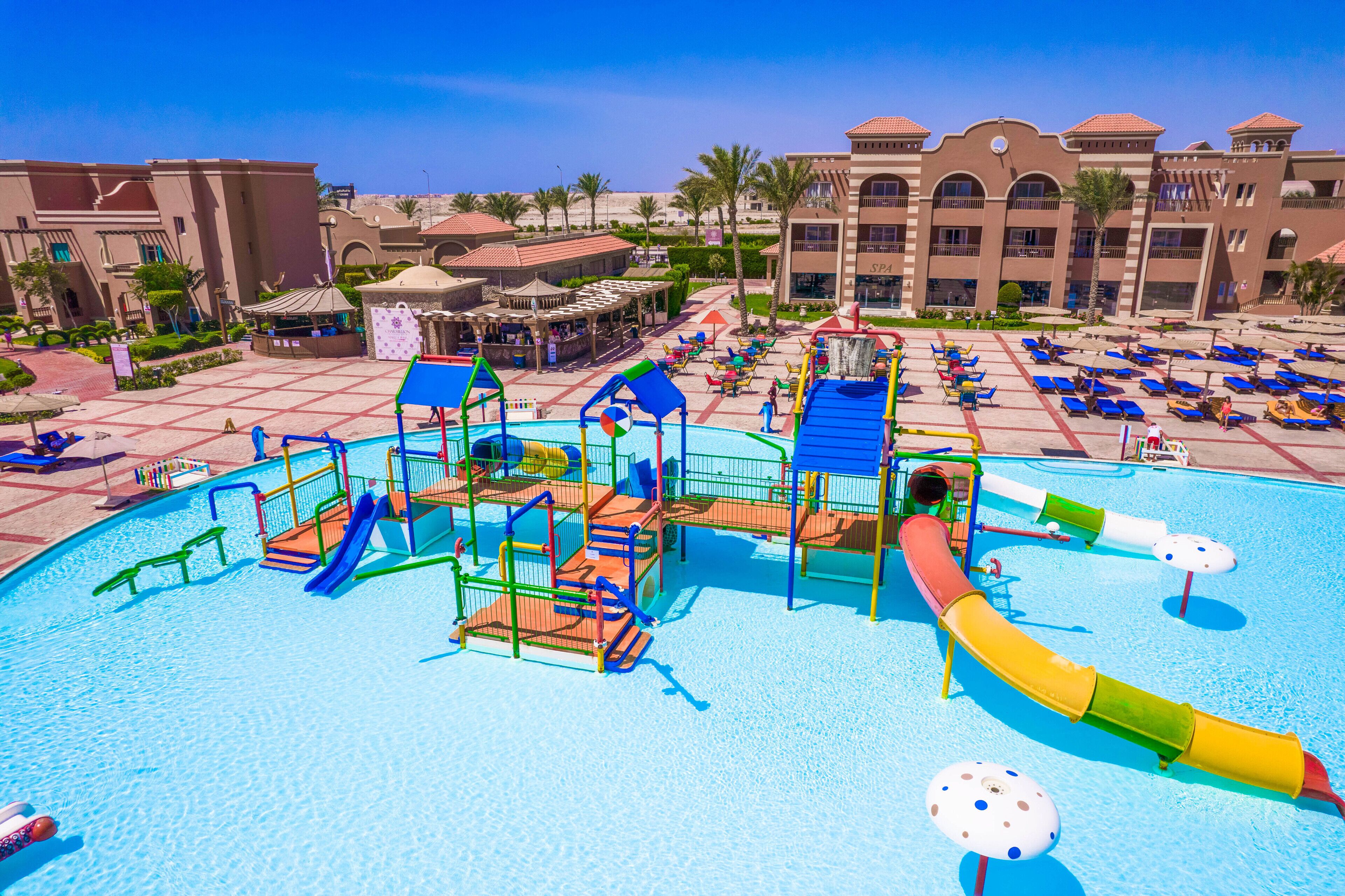 A water park area with slides and play structures, surrounded by a pool and lounge chairs.