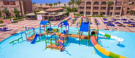 Zona de parque acuático con toboganes y estructuras de juego, rodeada por una piscina y tumbonas.
