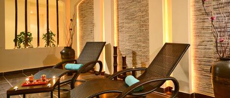 Un área de spa con dos sillones de mimbre, una mesita con velas y una pared decorativa con elementos verticales.