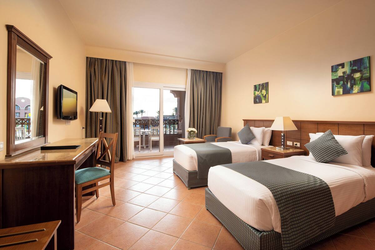 Une chambre d’hôtel avec deux lits, un bureau, une chaise, une télévision et une vue sur l’extérieur.