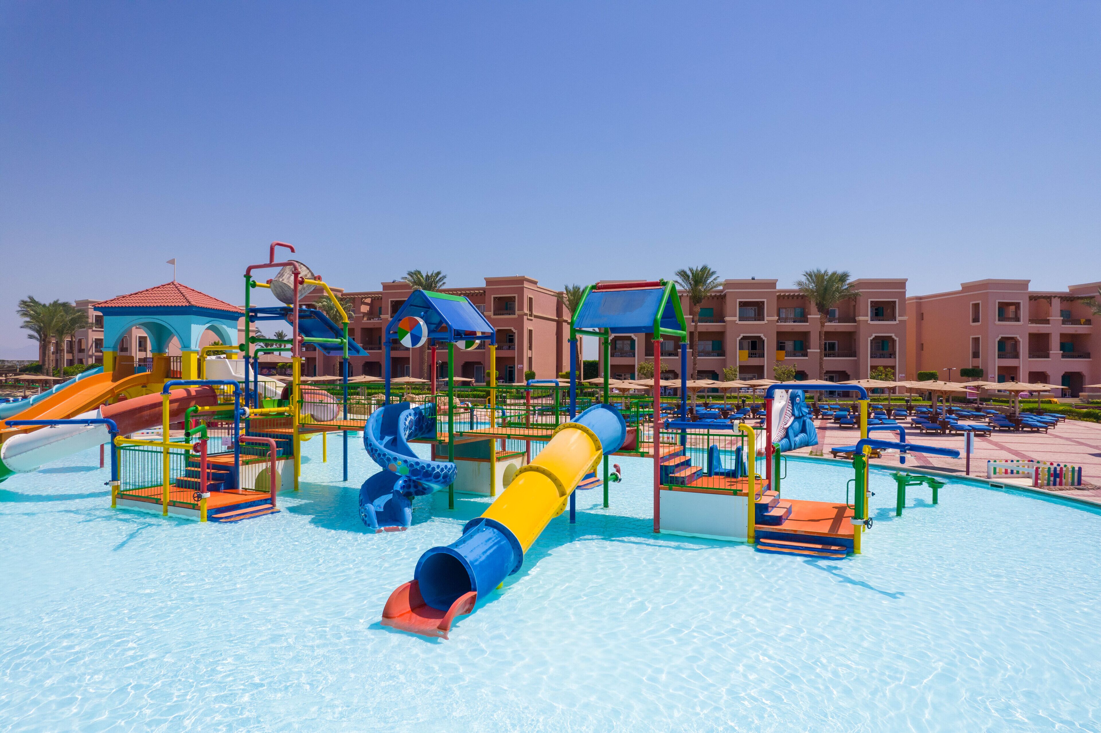 A water park with slides and play structures, surrounded by a pool and a building with balconies.