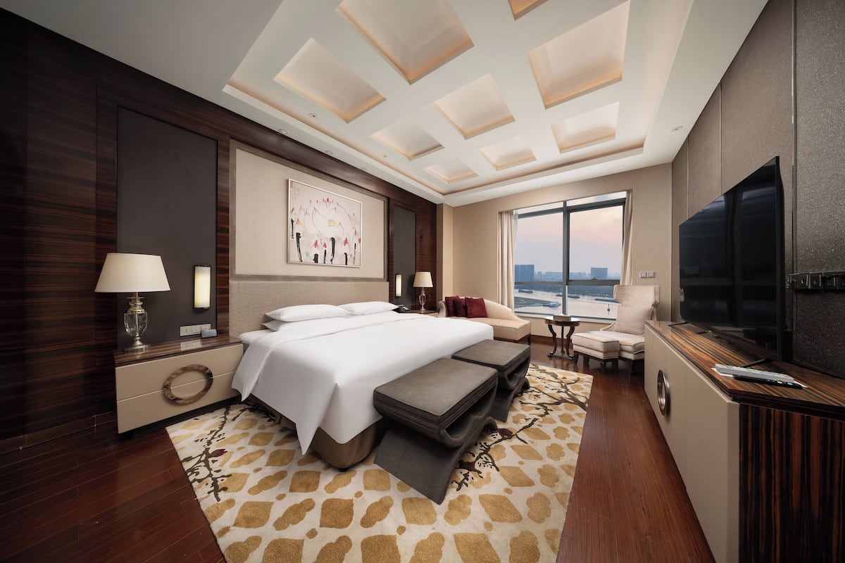 Habitación de hotel moderna con una cama grande, un sofá, un televisor y vistas a la ciudad.