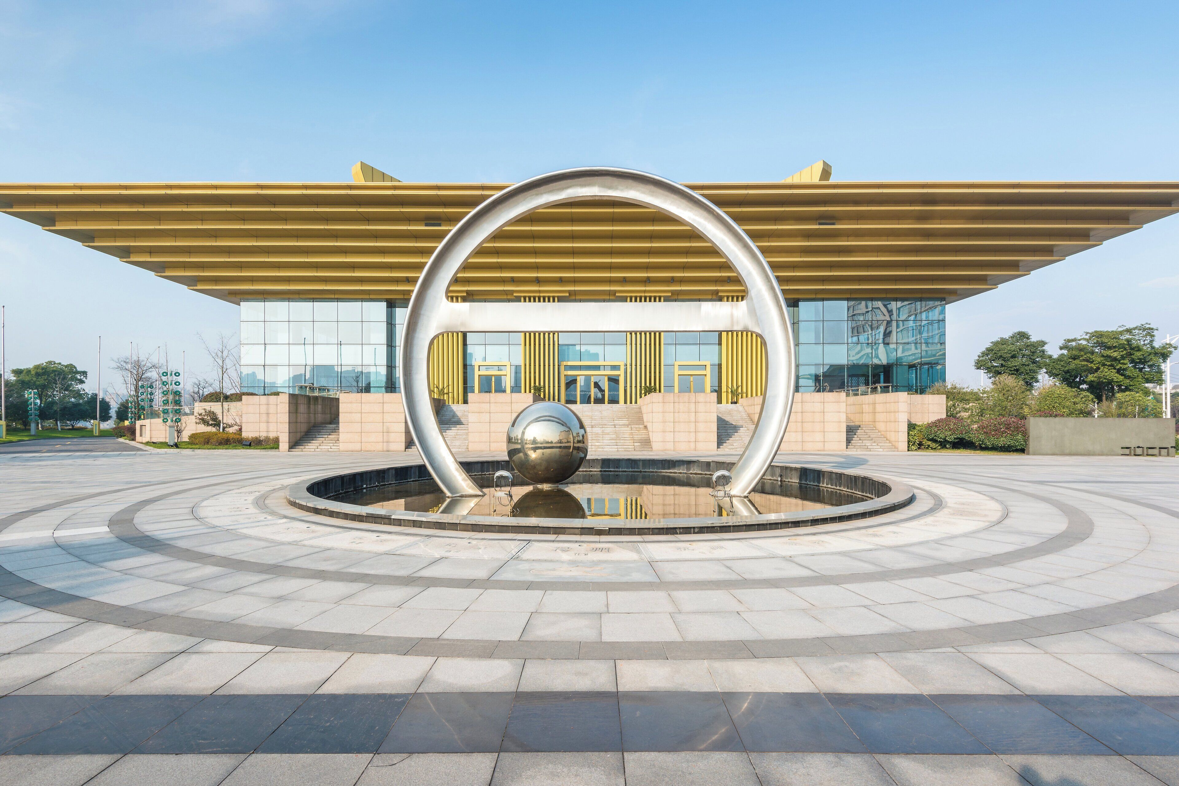 A modern building with a circular metallic sculpture in front.