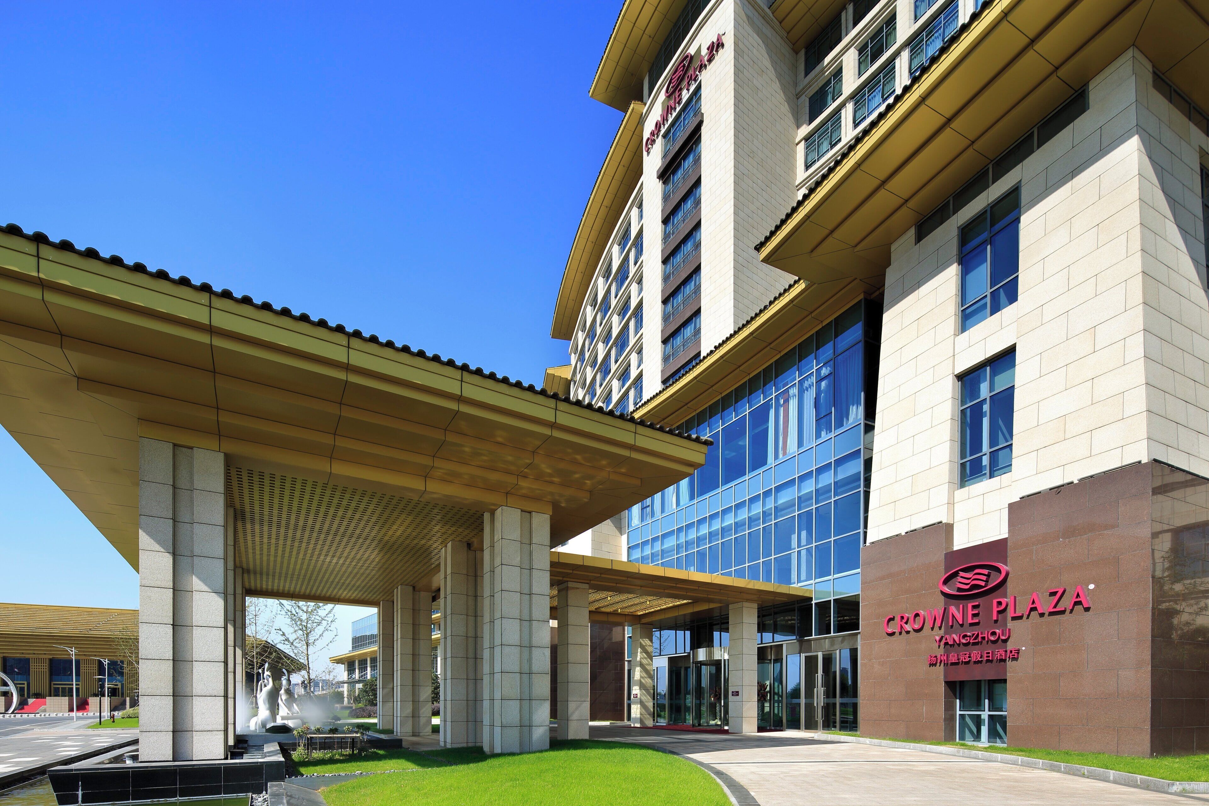 A modern building with a covered entrance area, large windows, and a prominent signage for Crowne Plaza Yangzhou.