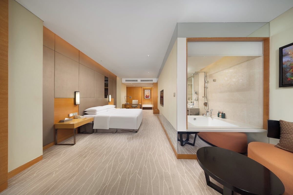 Una habitación de hotel moderna con una cama grande, un escritorio, una silla, un sofá y un baño con bañera y lavamanos.