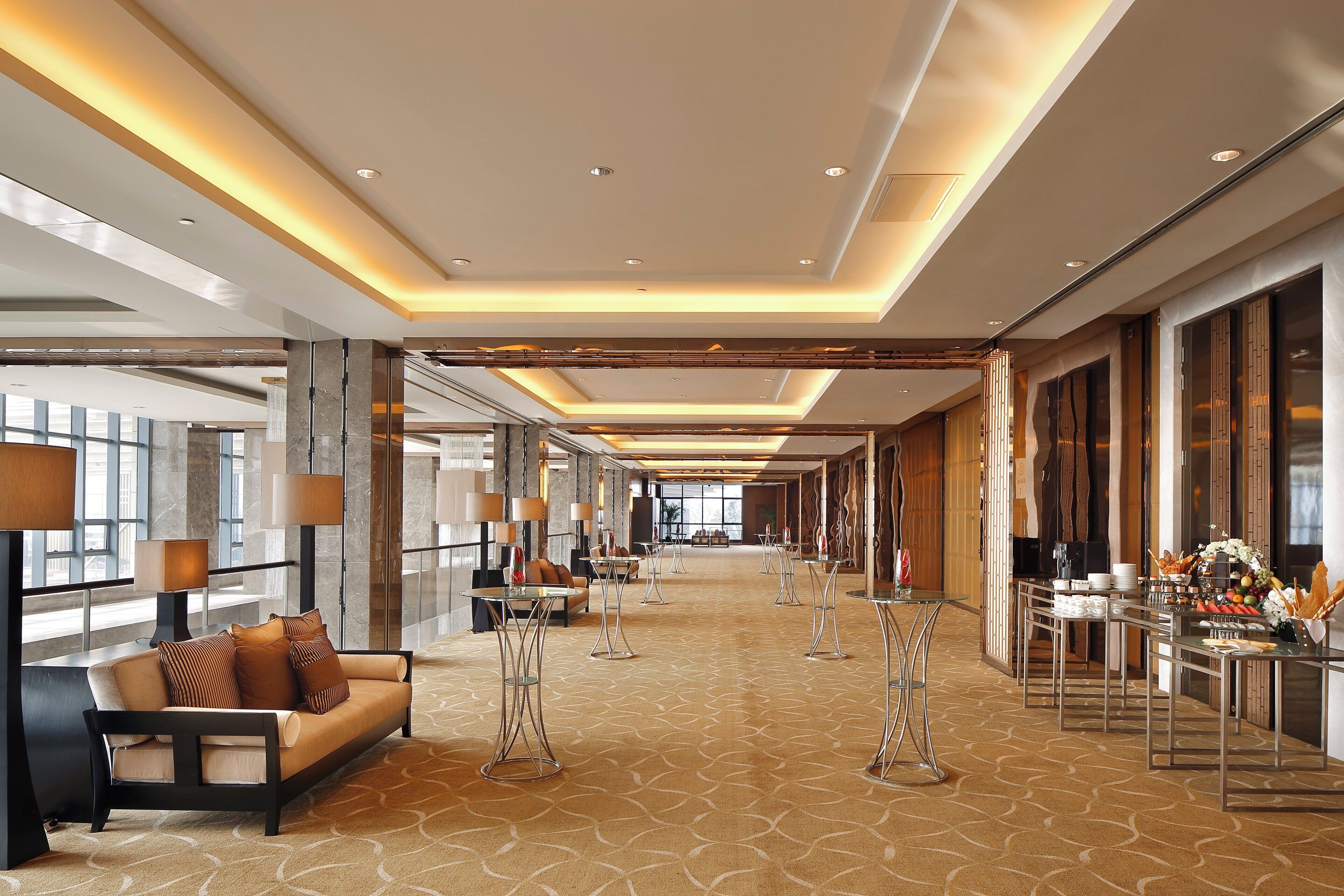 Un amplio hall de hotel con un largo pasillo, zonas de estar y una mesa de buffet.