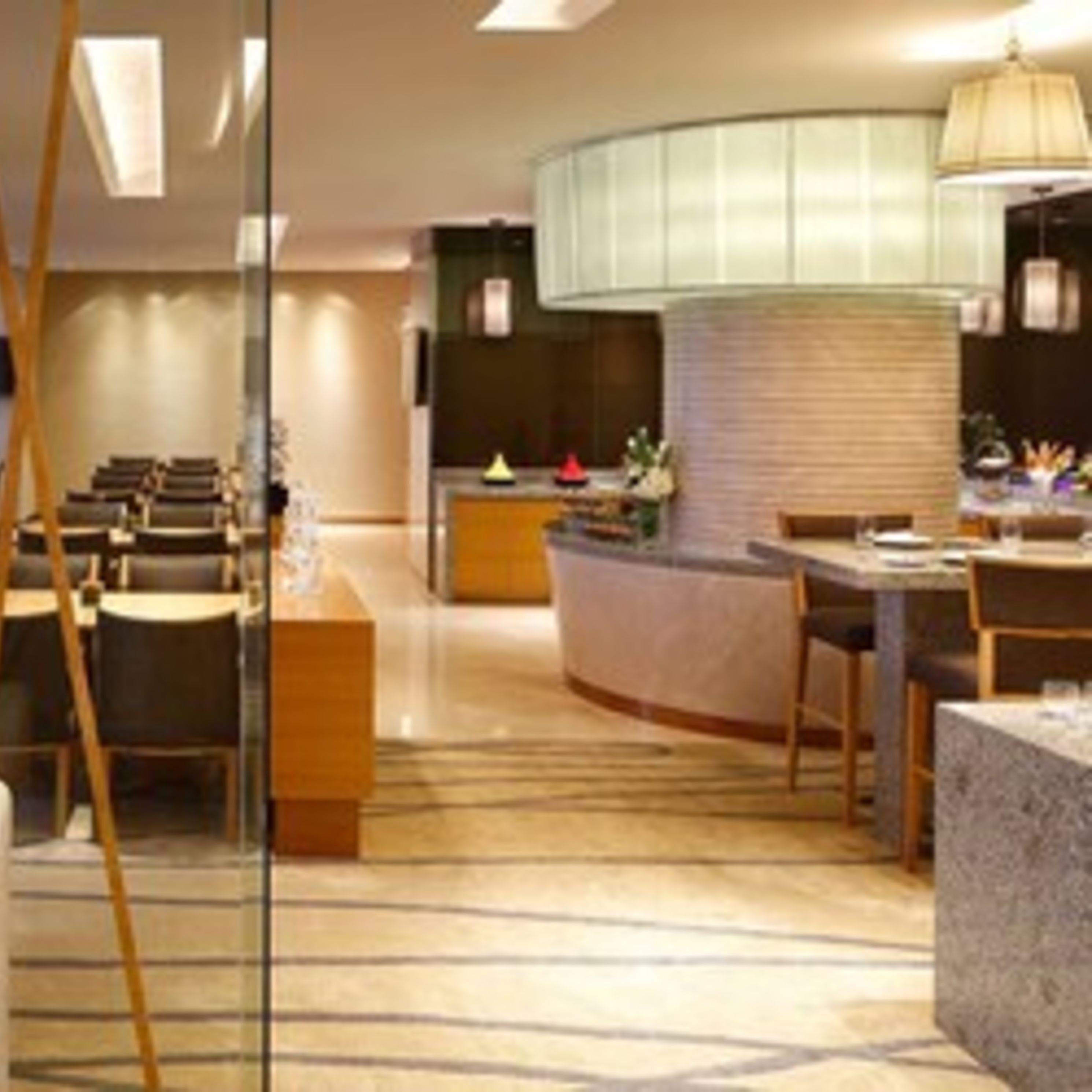 A modern hotel lobby with a curved reception desk, seating area with tables and chairs, and a patterned carpet.