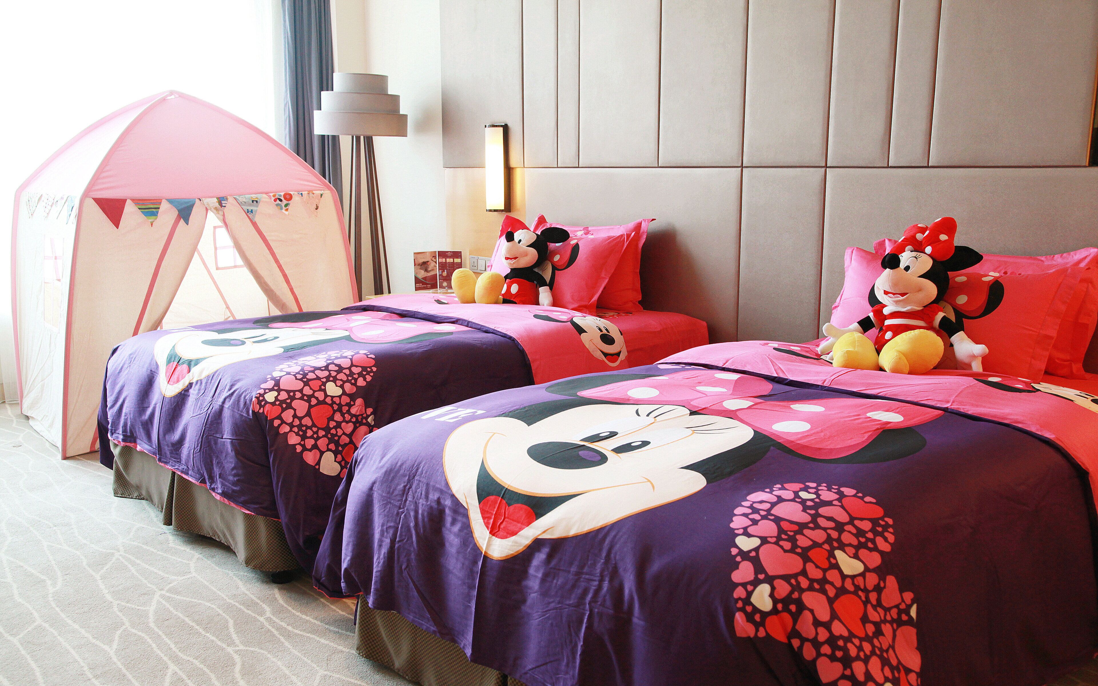 A hotel room with two beds, each adorned with Minnie Mouse themed bedding.