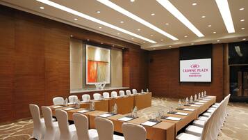 Een vergaderruimte met een lange tafel, witte stoelen en een projectorscherm waarop 'CROWNE PLAZA YANGZHOU' staat.