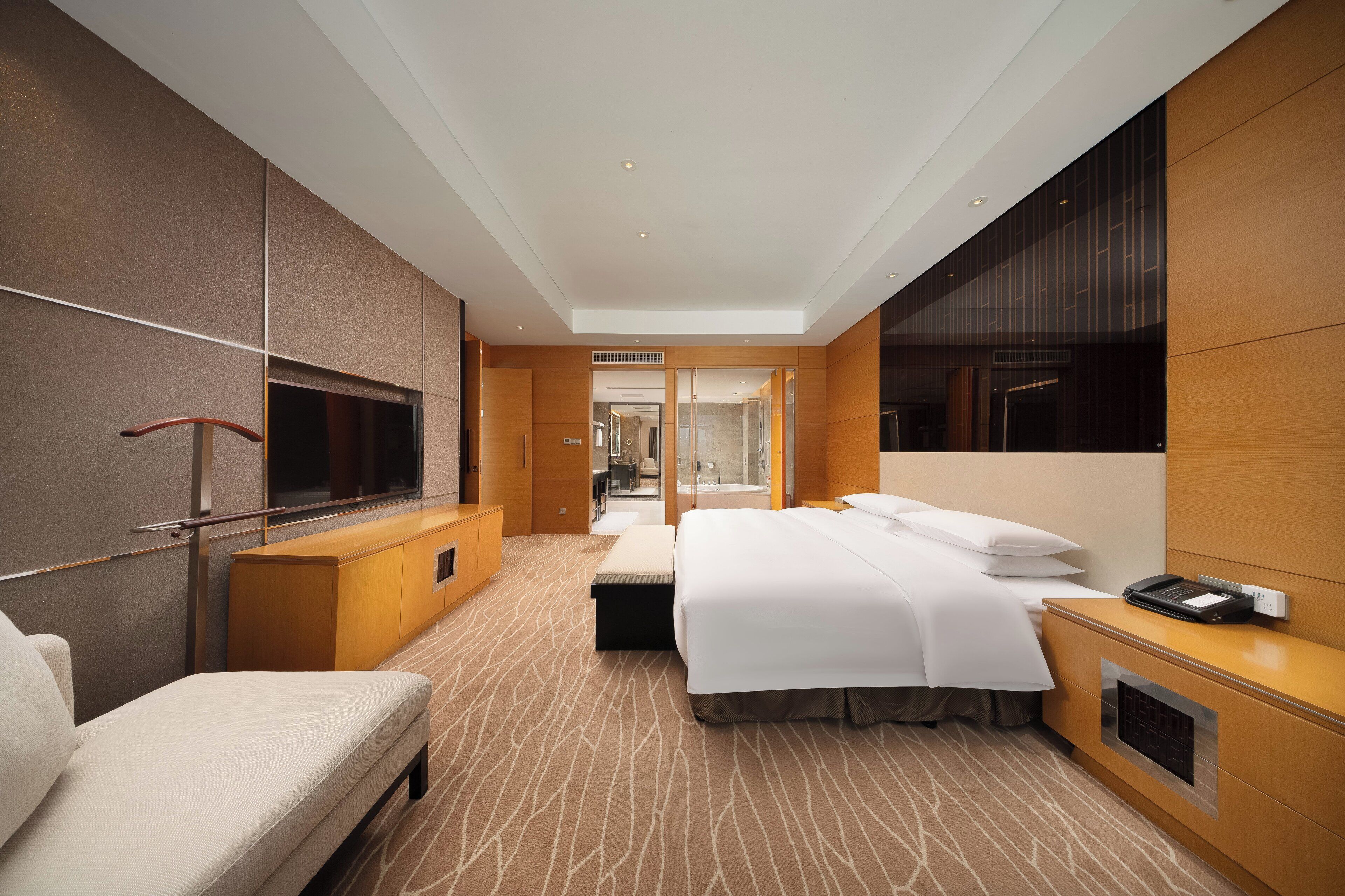 A modern hotel room with a large bed, a sofa, a TV, and a minibar.